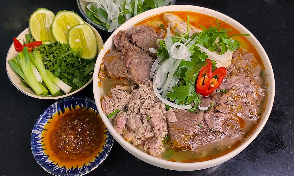 Tô bún bò Huế nóng hổi với chả cua, giò heo và rau sống.
