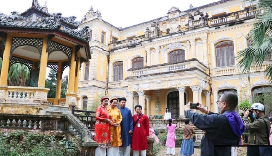 Một nhóm khách du lịch mặc trang phục truyền thống đứng chụp ảnh trước Cung An Định, một công trình kiến trúc mang phong cách châu Âu ở Huế.
