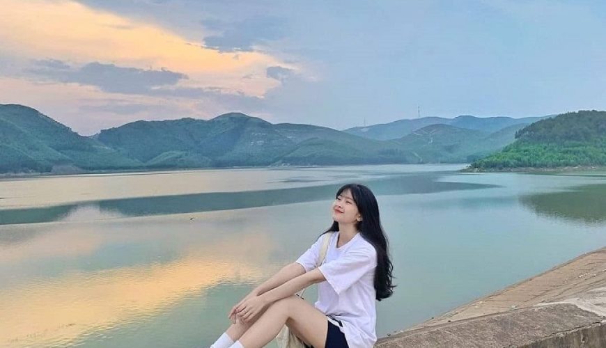 Một cô gái trẻ ngồi trên bờ đập ngắm cảnh hoàng hôn tại Hồ Khe Ngang.