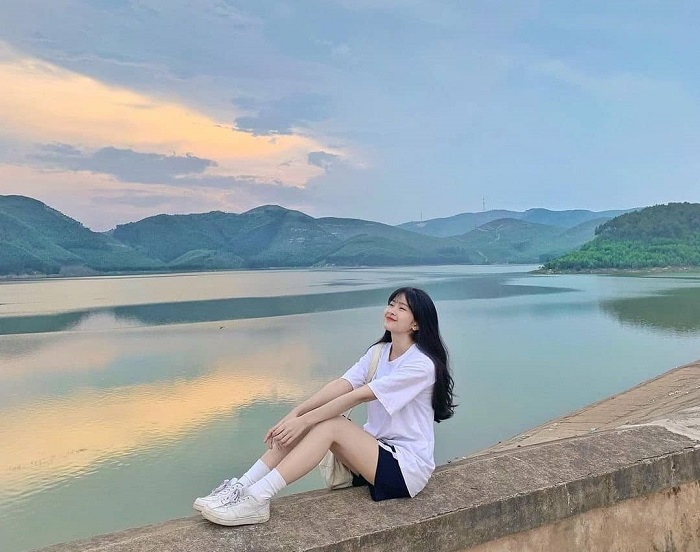 Một cô gái trẻ ngồi trên bờ đập ngắm cảnh hoàng hôn tại Hồ Khe Ngang.