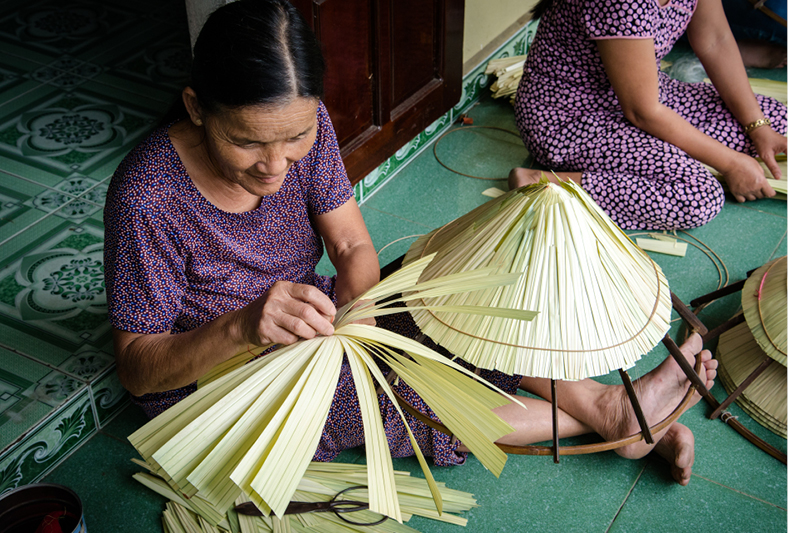 Một người thợ làm nón lá đang tỉ mỉ chằm từng đường kim mũi chỉ.