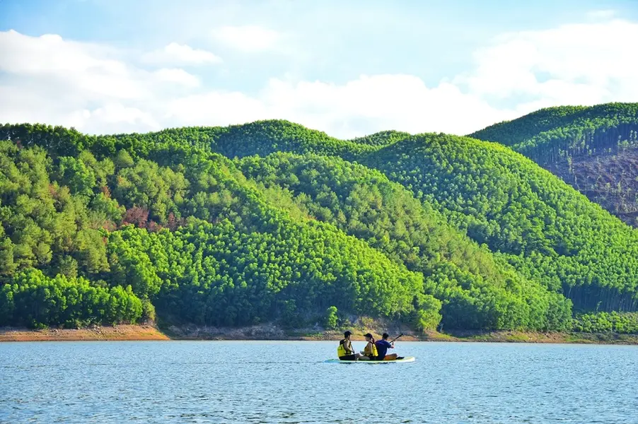 Ba người chèo thuyền kayak trên mặt hồ trong xanh, bao quanh bởi những ngọn đồi phủ đầy cây.