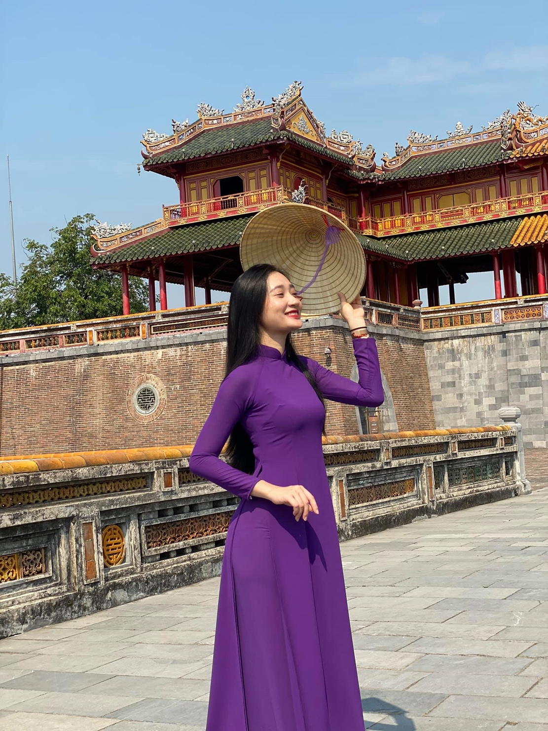 Một người phụ nữ lớn tuổi mặc áo dài tím Huế đang đi dạo trên đường.