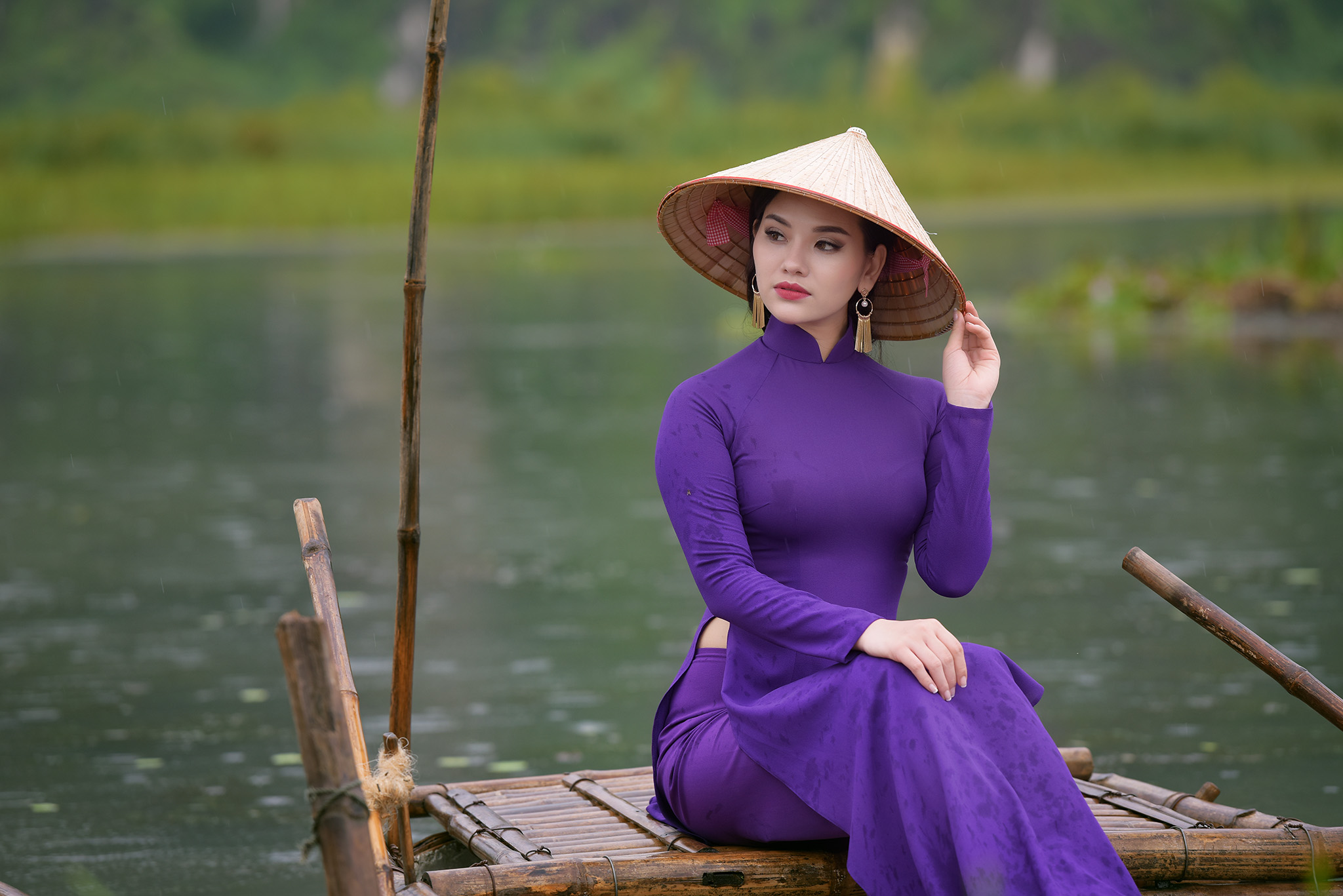 Một cô gái Huế duyên dáng mặc áo dài tím truyền thống, đội nón lá, đứng bên bờ sông Hương.