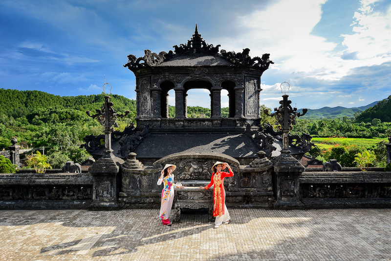 Cảnh quan một lăng cổ kính ở Huế dưới ánh nắng vàng nhẹ nhàng, có vài du khách đang tham quan.