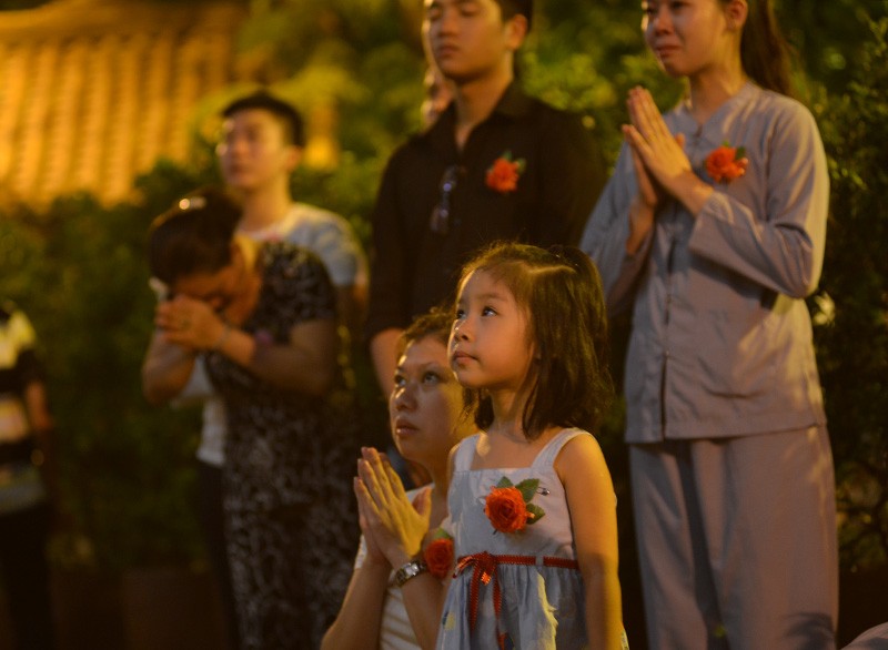 Một cô bé người Việt Nam đứng cùng gia đình trong một nghi thức tôn giáo, với bông hồng cài trên ngực áo.