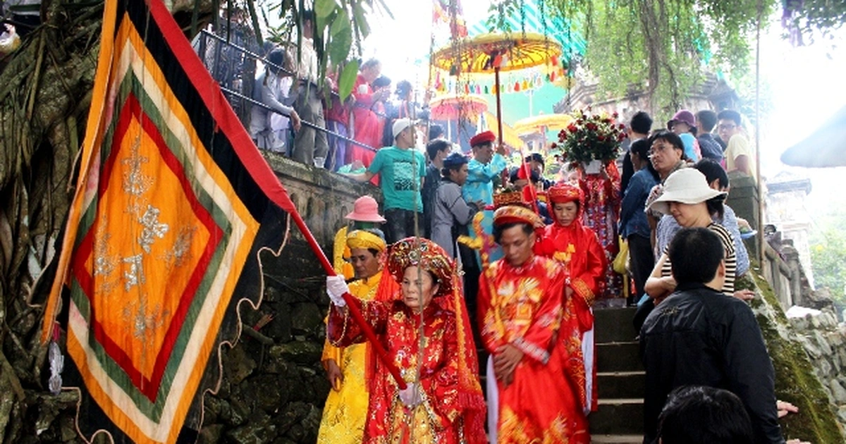 Đoàn người mặc trang phục cung đình màu đỏ và vàng, cầm cờ và lọng, đang di chuyển trên bậc đá lên Điện Hòn Chén.