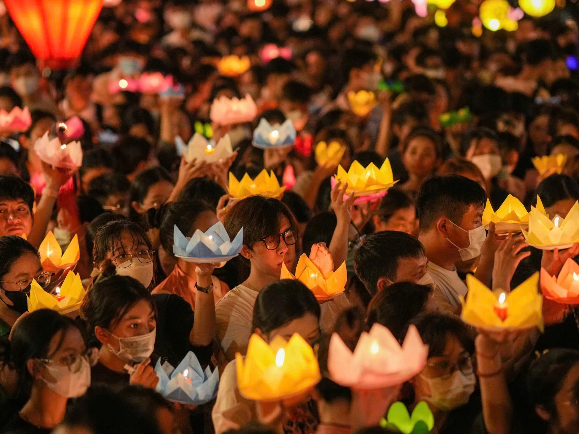 Một đám đông người dân và Phật tử ở Việt Nam tham gia một nghi lễ tôn giáo, tay cầm những chiếc đèn hoa sen phát sáng.