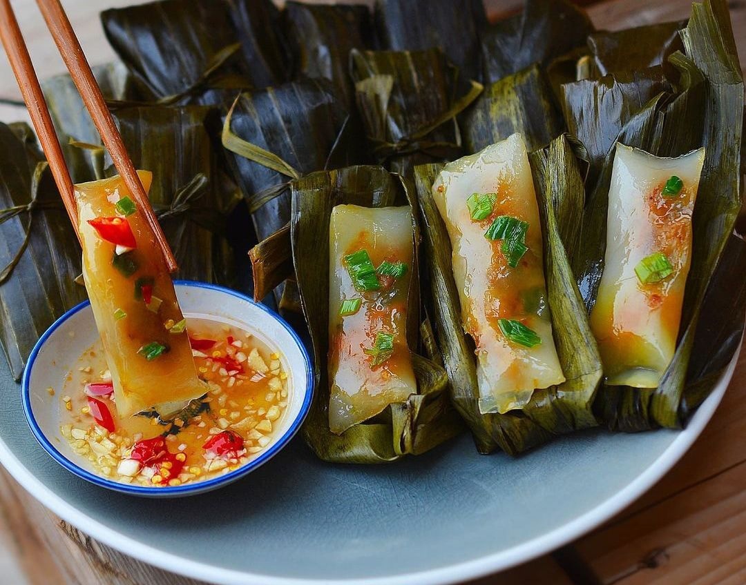 Cận cảnh một đĩa bánh bèo và bánh lọc, món ăn đặc trưng của ẩm thực Huế. Một đôi đũa đang gắp một chiếc bánh lọc để chấm vào bát nước mắm.